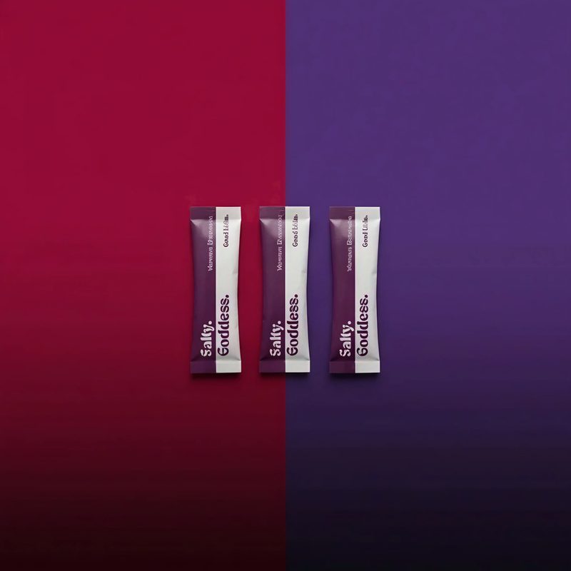 Three Salty Goddess stick packs on a red and purple background